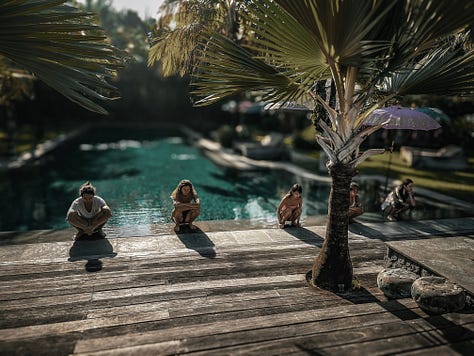 Group practicing squat position at tropical pool yoga retreat