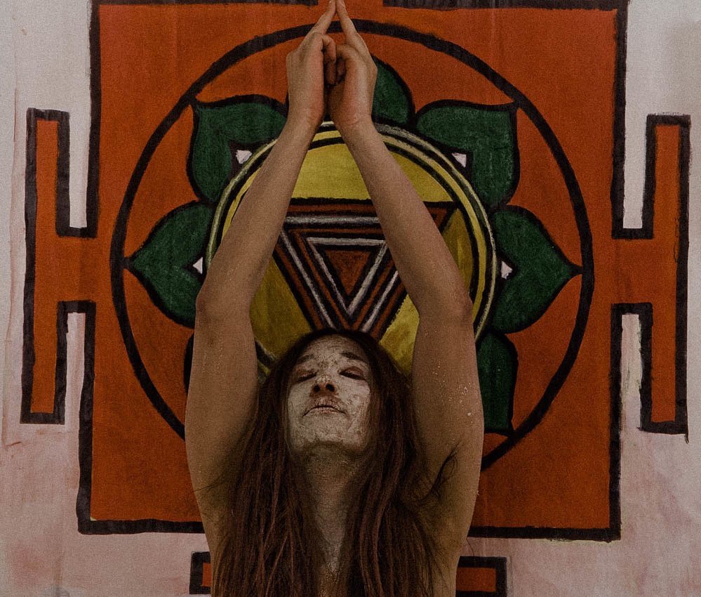 Woman with white ritual face paint and raised arms before tantric Sri Yantra mandala - sacred ceremony and goddess invocation