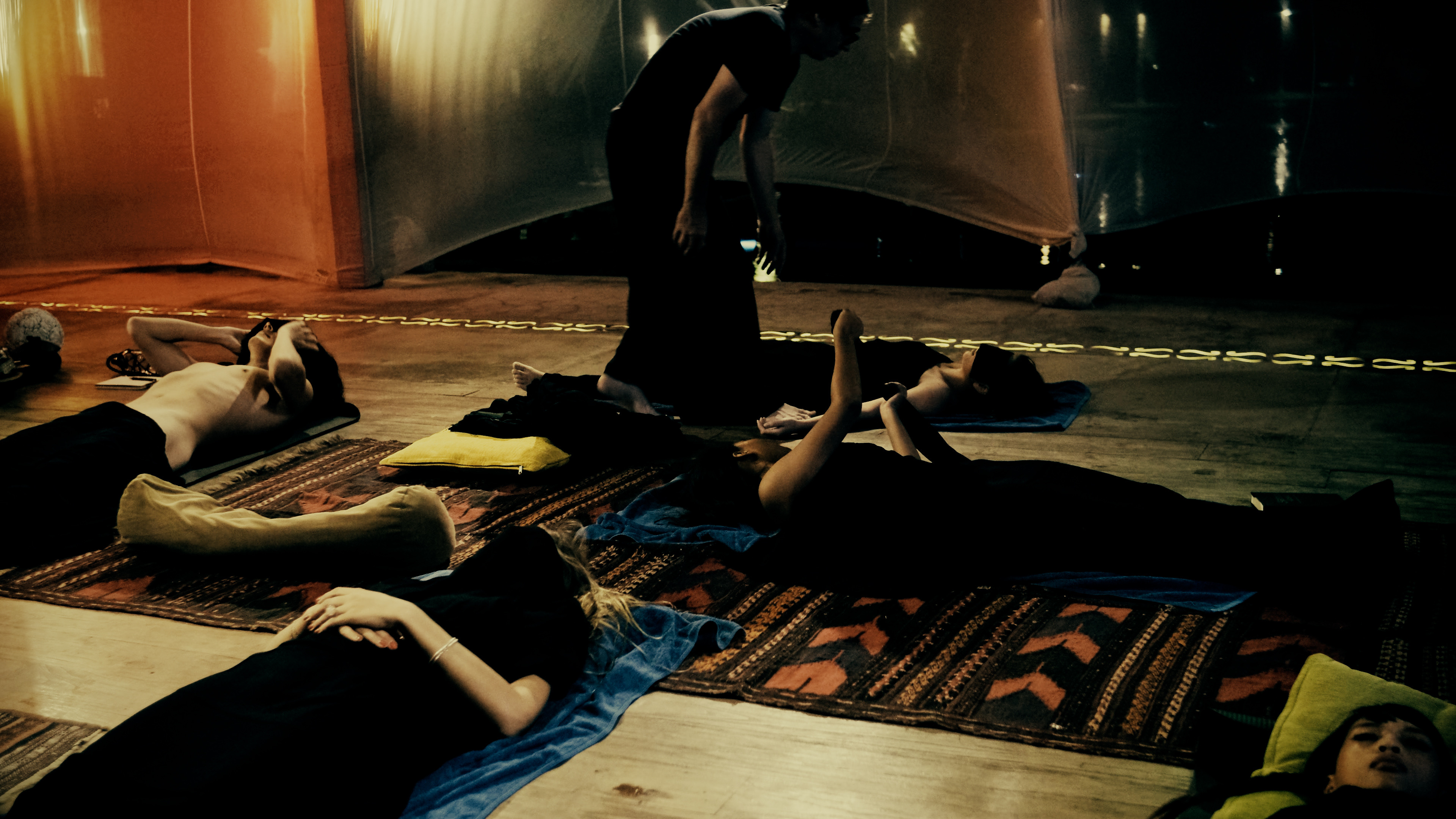Group tantra retreat participants lying on traditional rugs during breathwork session with instructor guiding - Sensual Liberation Retreat practice